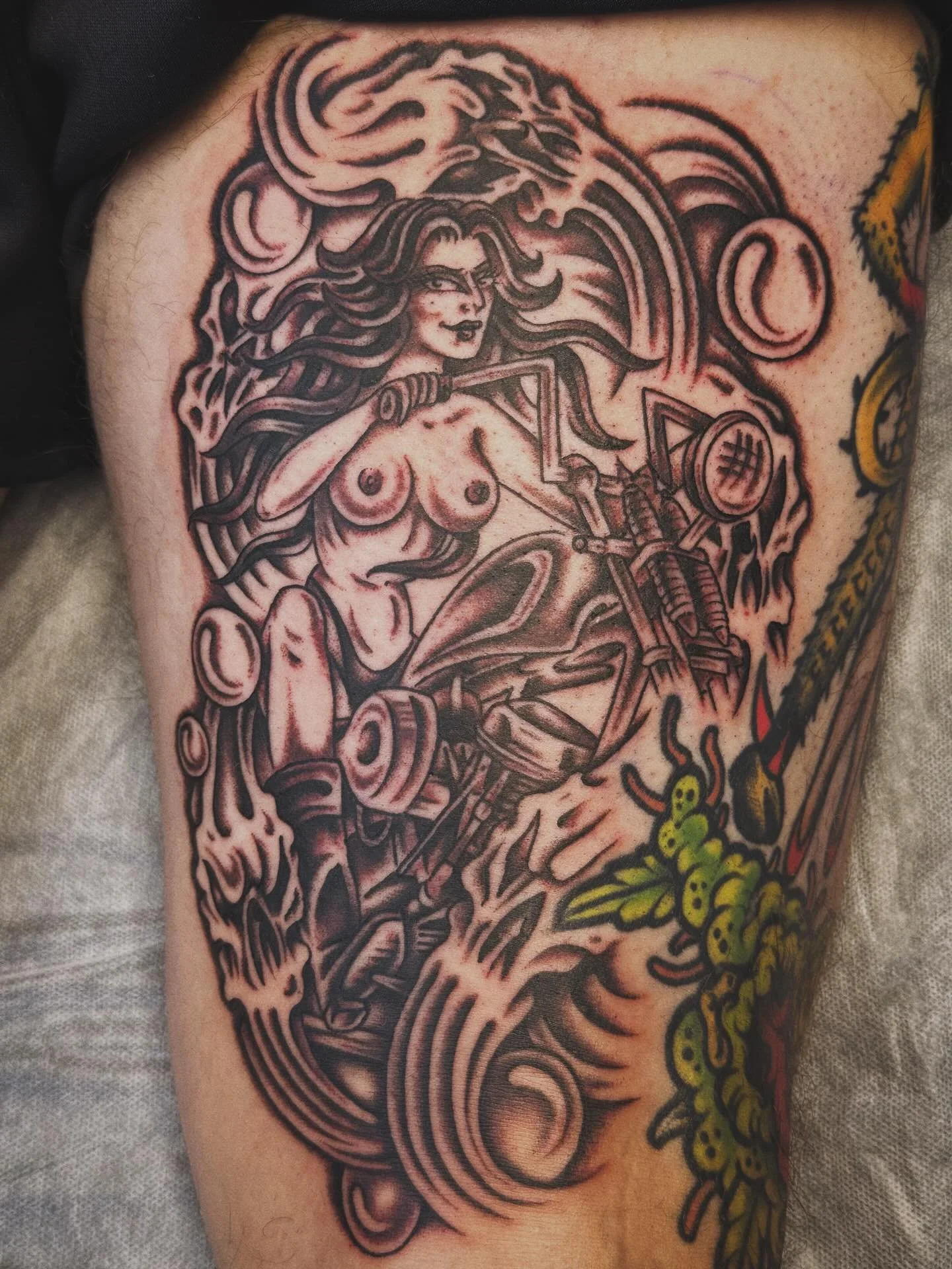 Black and gray tattoo of a woman with flowing hair riding a motorcycle, surrounded by swirling patterns and abstract elements.