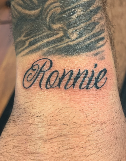 Tattoo of the name "Ronnie" in cursive on a person's wrist.