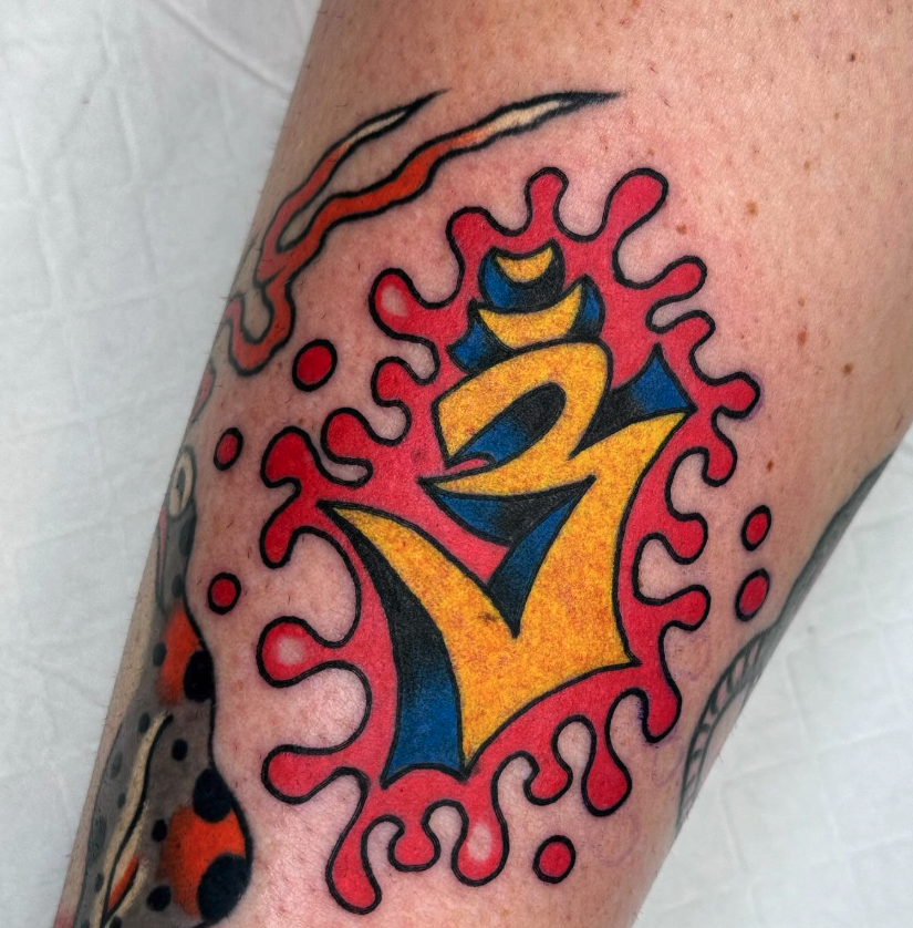 A colorful tattoo featuring stylized yellow and blue characters, surrounded by red and pink abstract shapes and black outlines.