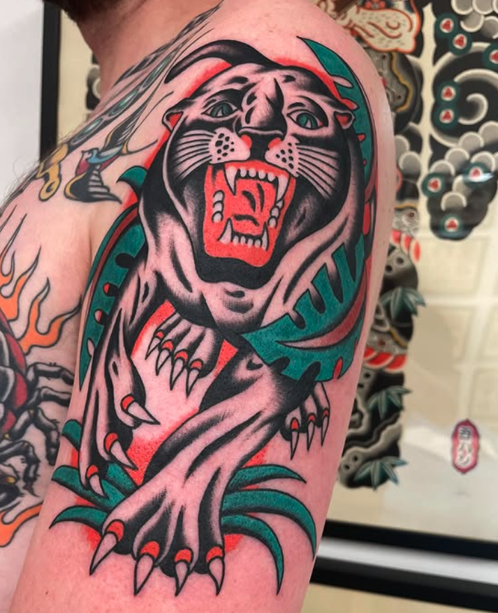 Traditional-style tattoo of a fierce black panther with green eyes, snarling, with sharp claws and red accents.