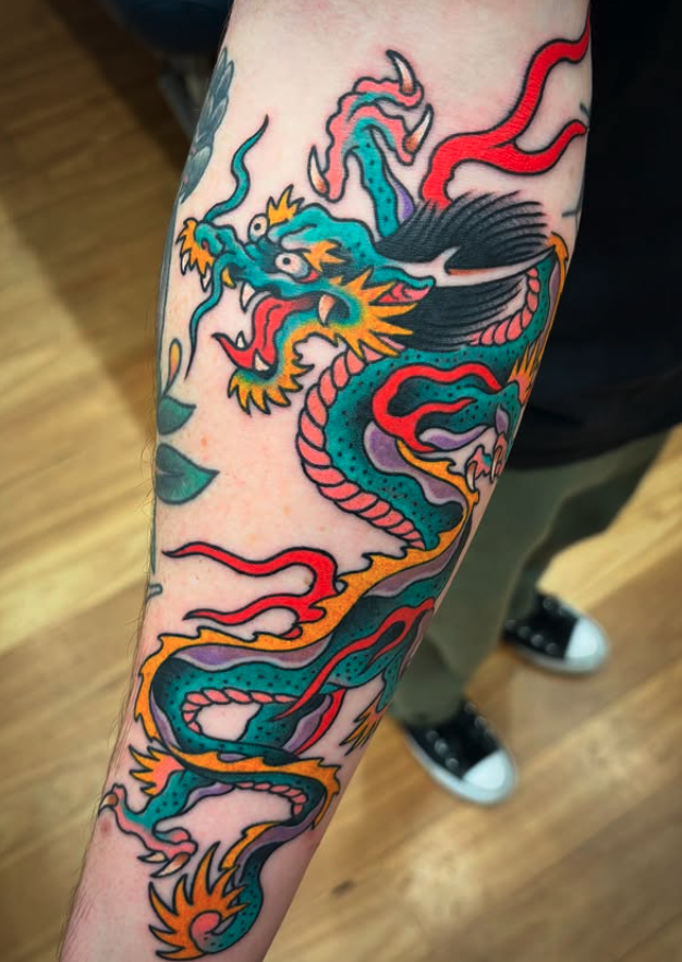 Colorful dragon tattoo on person's arm with traditional Japanese style, featuring a fierce dragon with a long, winding body, sharp claws, and vibrant colors including blue, yellow, red, purple, and black.