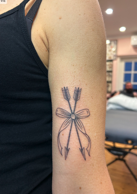Tattoo of two crossed arrows and a bow on person's upper arm.