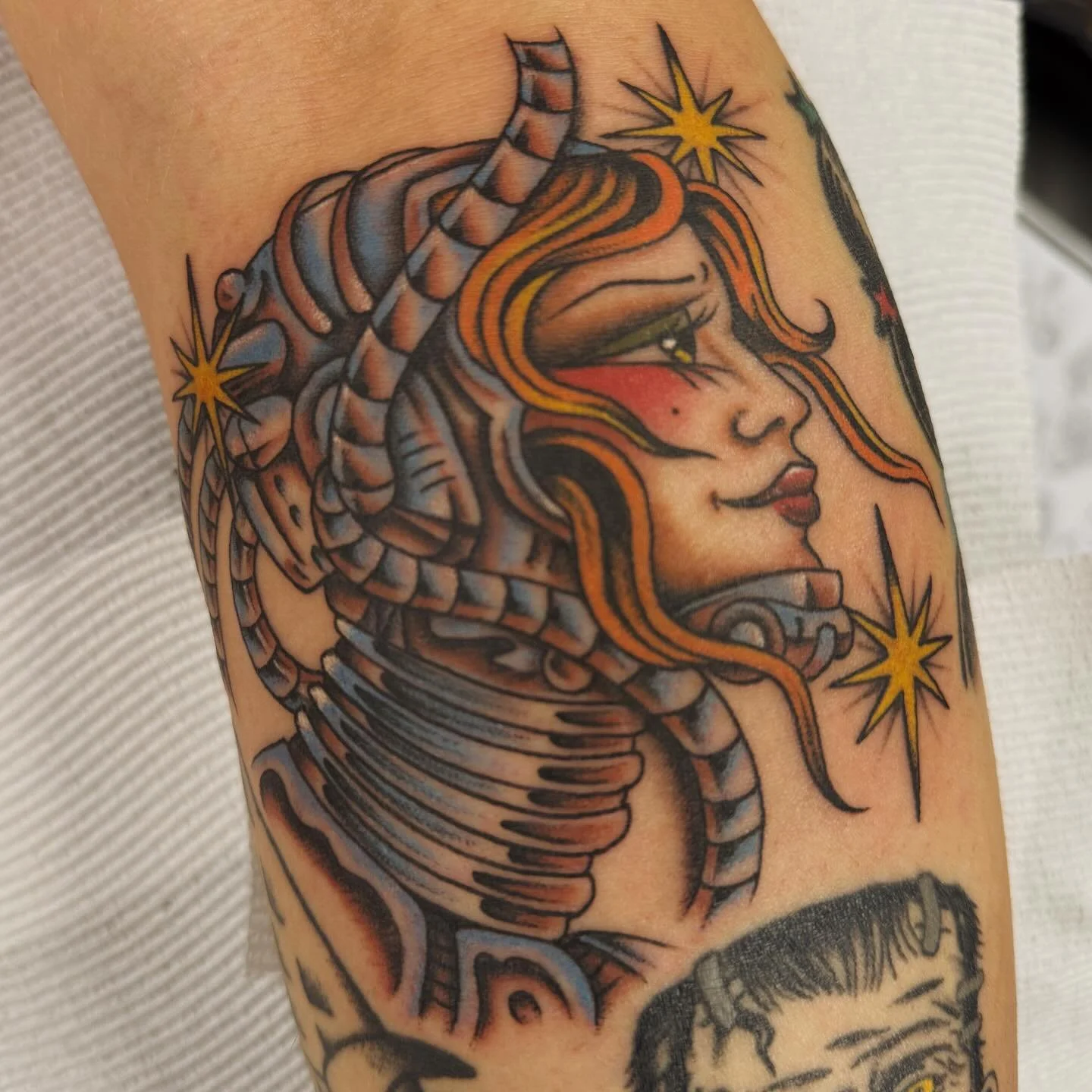 Tattoo of a woman's face with flowing hair, surrounded by stars and mechanical elements, in a traditional tattoo style.