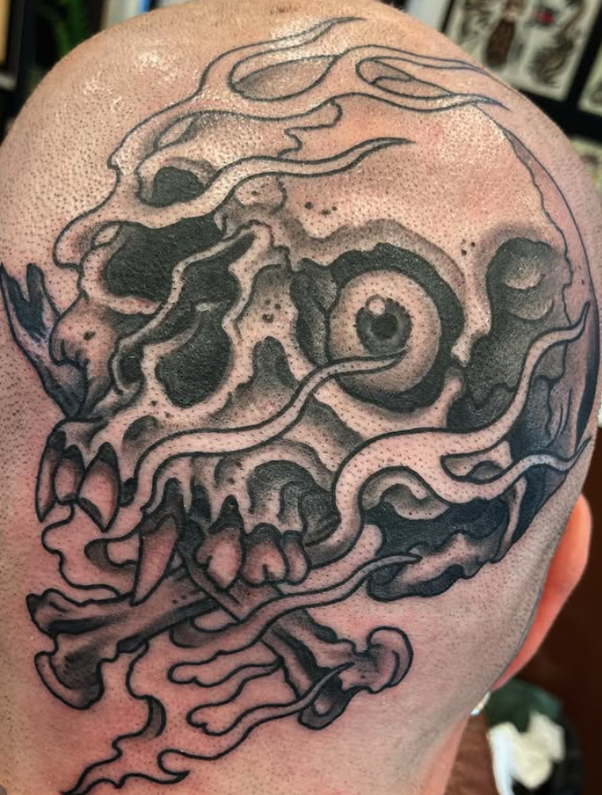 Tattoo of a stylized skull with swirling lines and abstract elements on a person's shoulder.