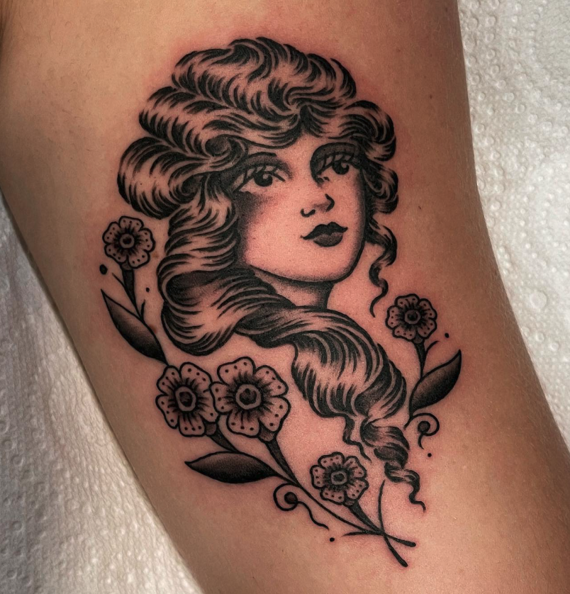 Black and gray tattoo of a woman's face with long, wavy hair surrounded by flowers.