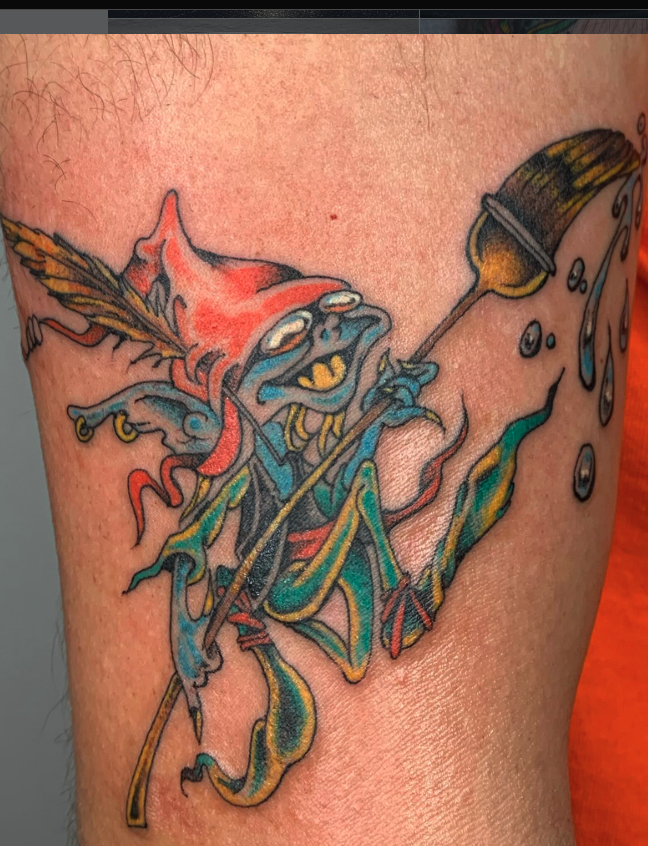 A colorful tattoo of a whimsical, cartoonish goblin holding a paintbrush dripping with paint or ink.