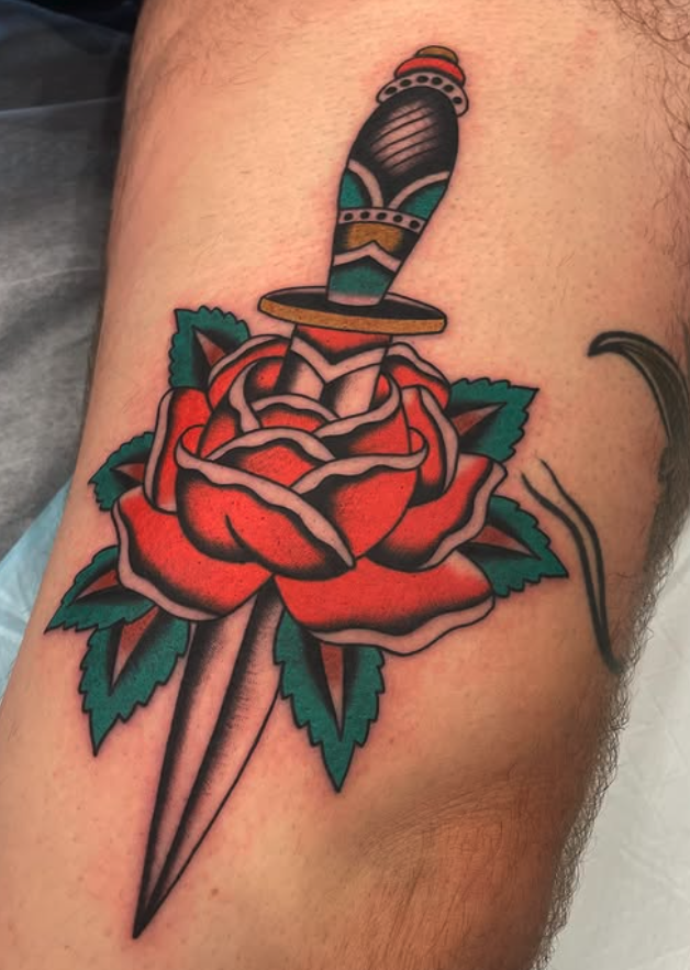 Tattoo of a dagger piercing through a red rose with green leaves.