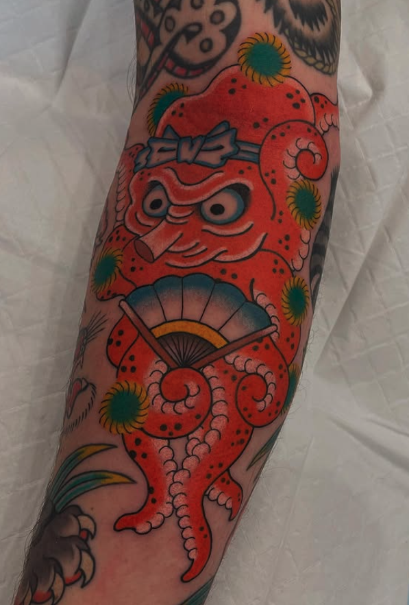 Colorful tattoo of an orange octopus with a fan over its head, surrounded by green and yellow circular accents on a person's forearm.