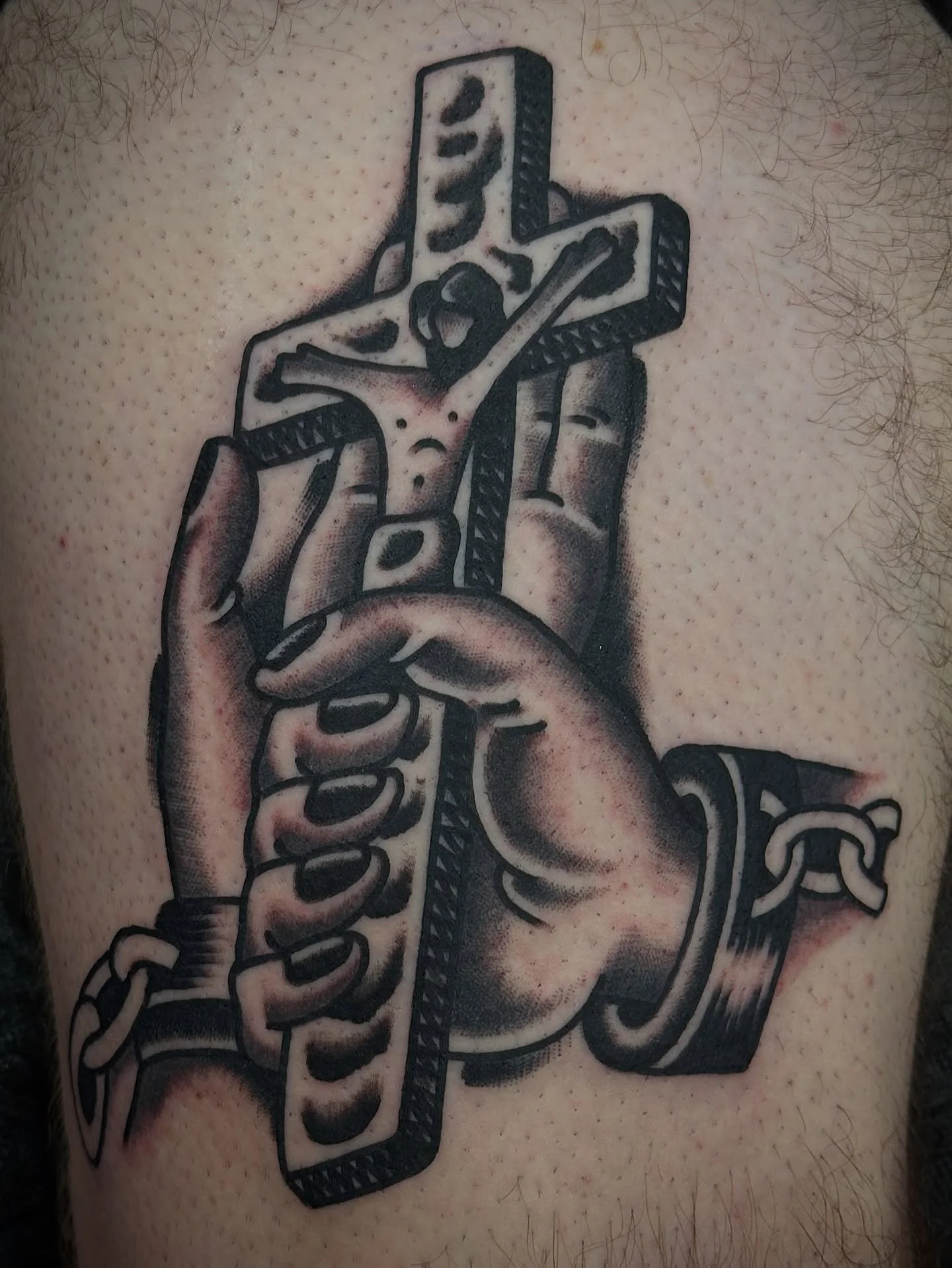 Tattoo of a realistic hand gripping a wooden crucifix with a figure of Jesus Christ, with the hand and crucifix detailed in black and gray ink.