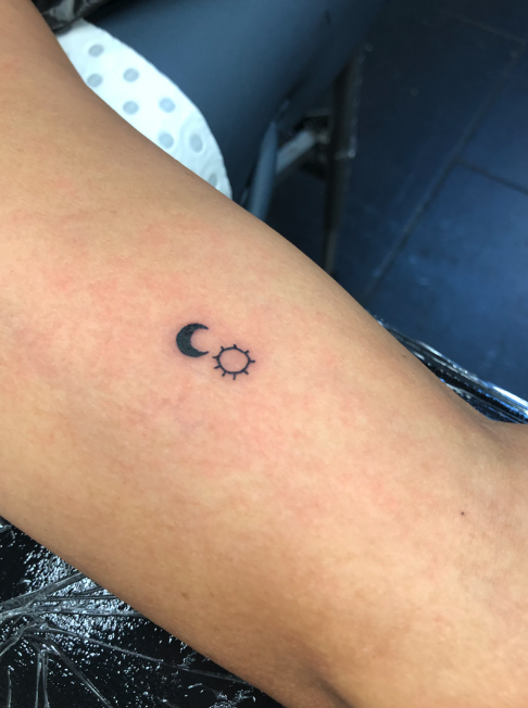 Tattoo of a crescent moon and a sun on a person's forearm.