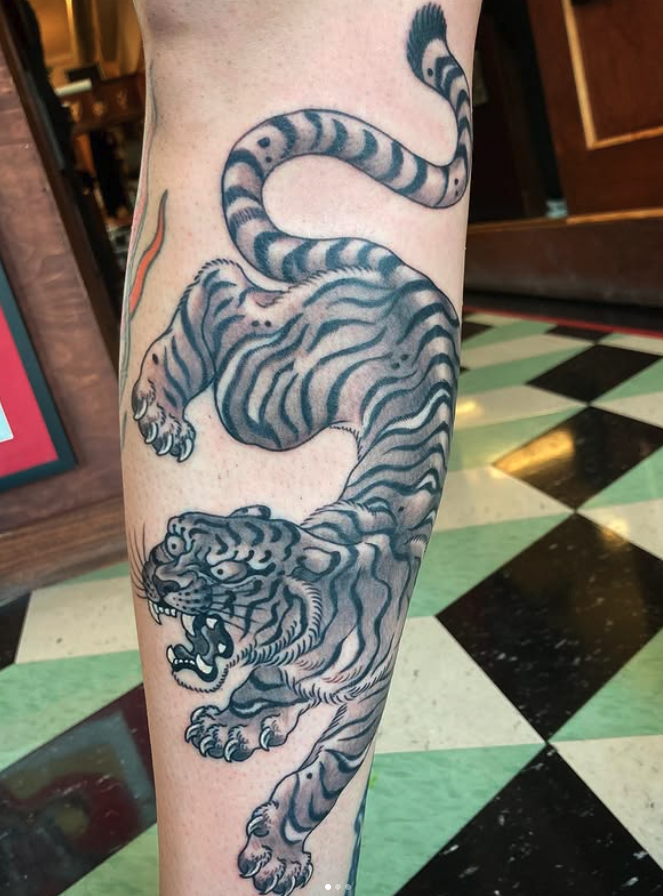 Tattoo of a roaring tiger with black and white stripes on a person's arm, with a stylized snake above the tiger.