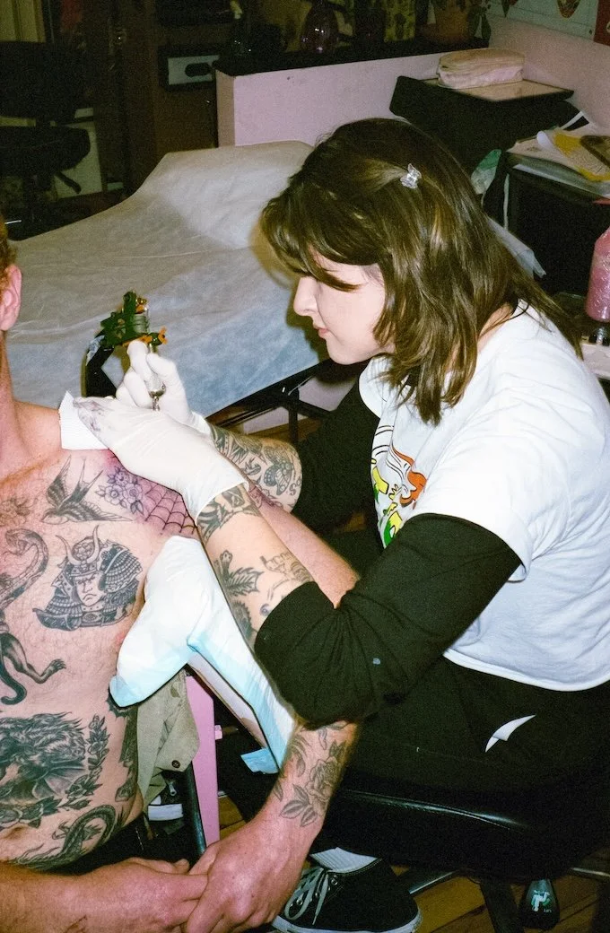 Tattoo artist tattooing a person's chest with various tattoos visible on his body.