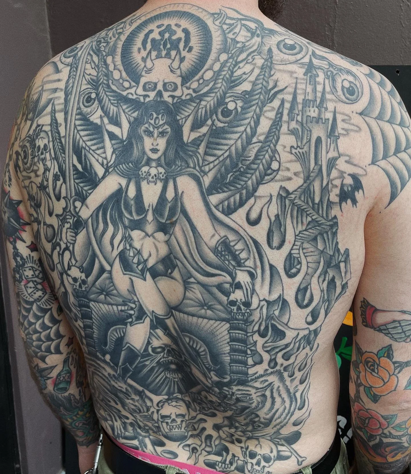 Black and gray tattoo of a fantasy female warrior with a sword, skulls, a castle, and a demon wing on the chest and upper body