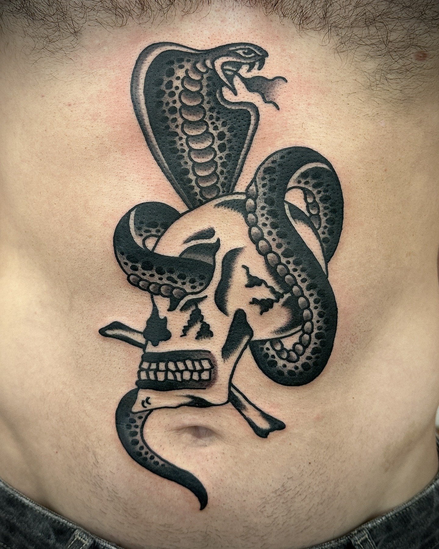 Tattoo of a human skull with a snake wrapped around it, with the snake's head extending upward with its tongue out.