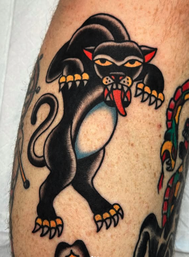 Tattoo of a black panther with a cat face, yellow eyes, and tongue sticking out, on person's upper arm.