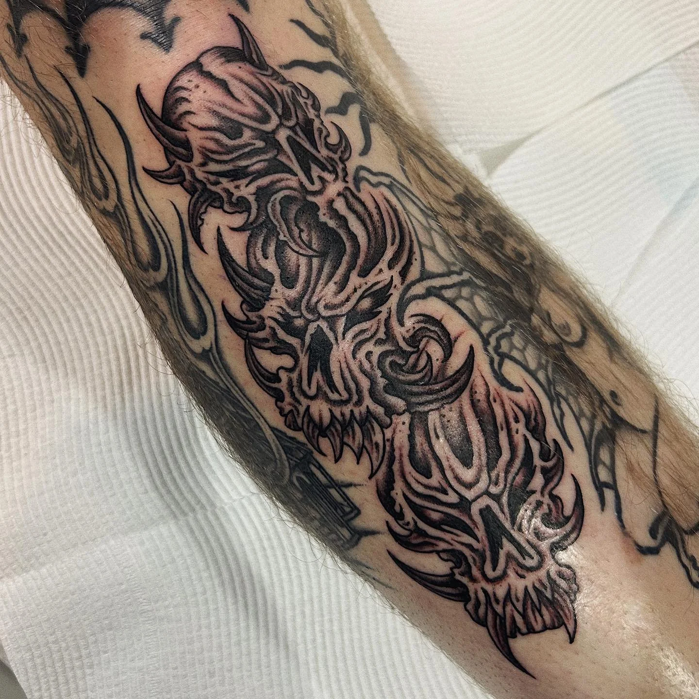 Tattoo of a demonic skull with horns, flames, and tribal patterns on a person's arm.