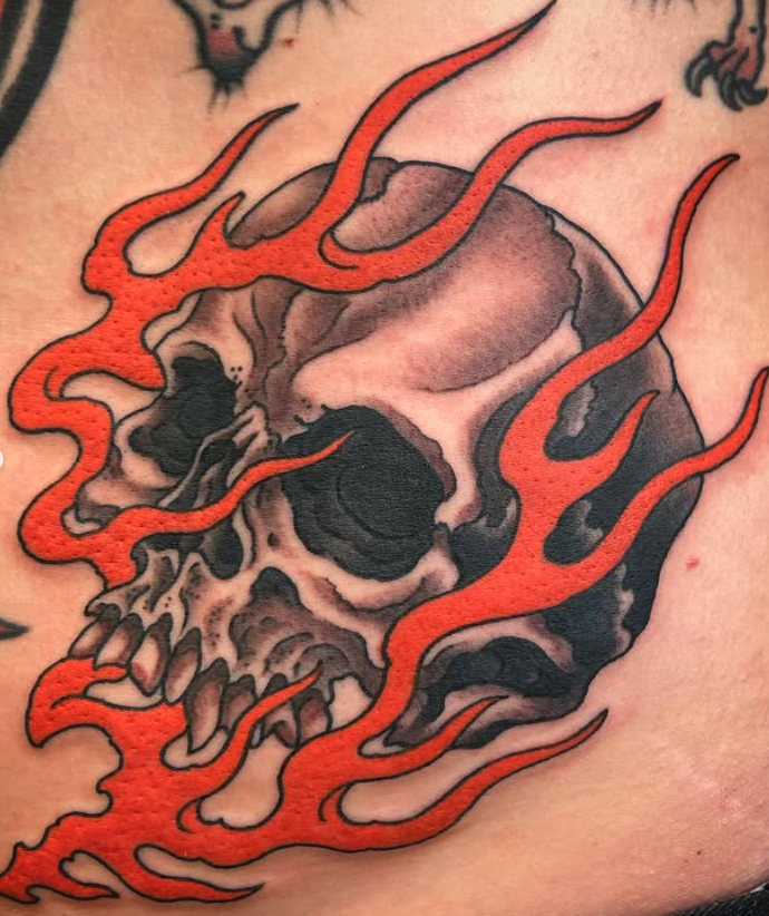 Tattoo of a human skull surrounded by red flames.