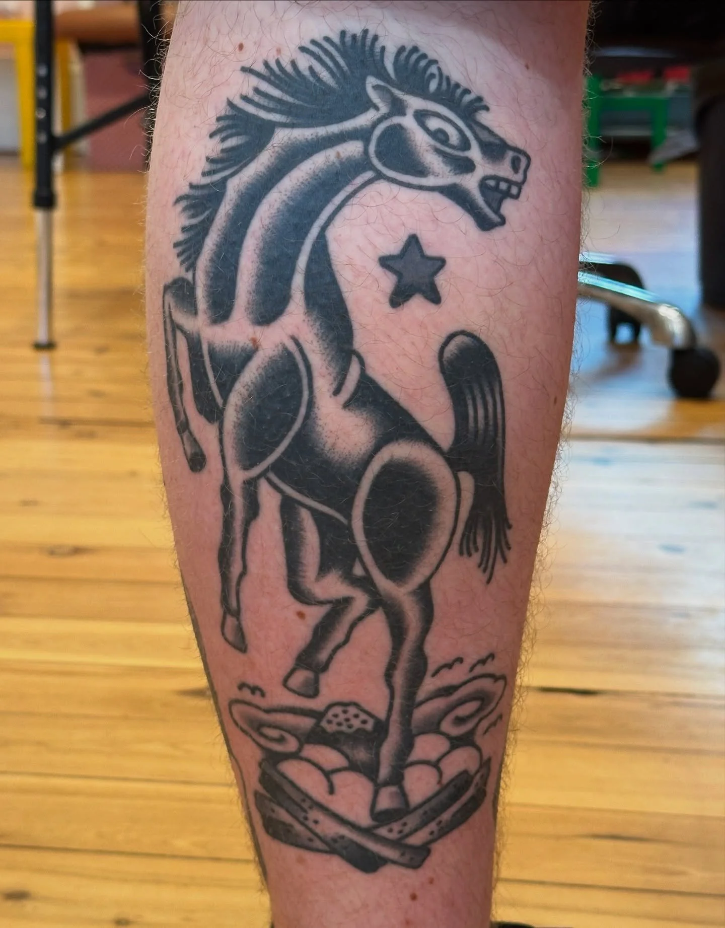 Black tattoo of a horse with a stylized, abstract design, a star and a oval shape near its head, and a spaceship at the bottom, on a person's leg.