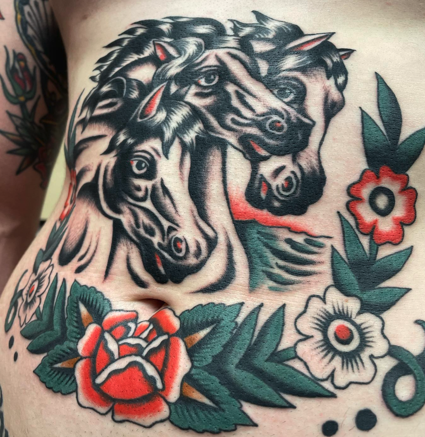 Tattoo of two fierce-looking, stylized black and gray horses with red accents, surrounded by colorful flowers and leaves on skin.