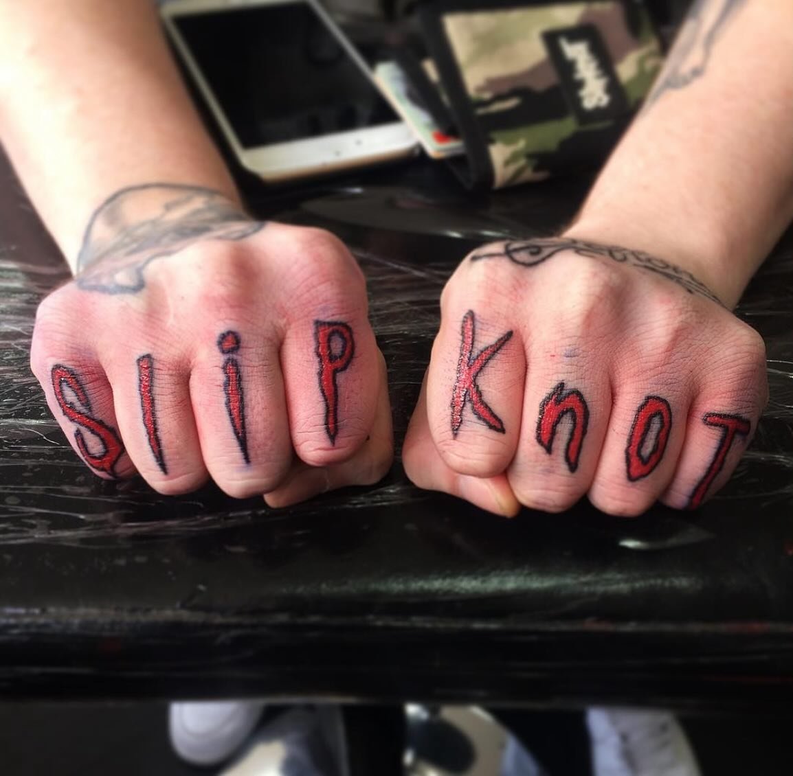 Tattoos on clenched fists spelling out 'sip' on the left hand and 'knot' on the right hand.