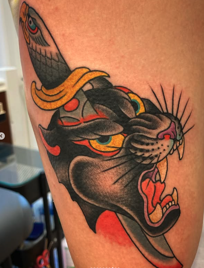 Tattoo of a fierce black panther with yellow eyes showing its teeth, and a koi fish above its head, in traditional style, on a person's skin.