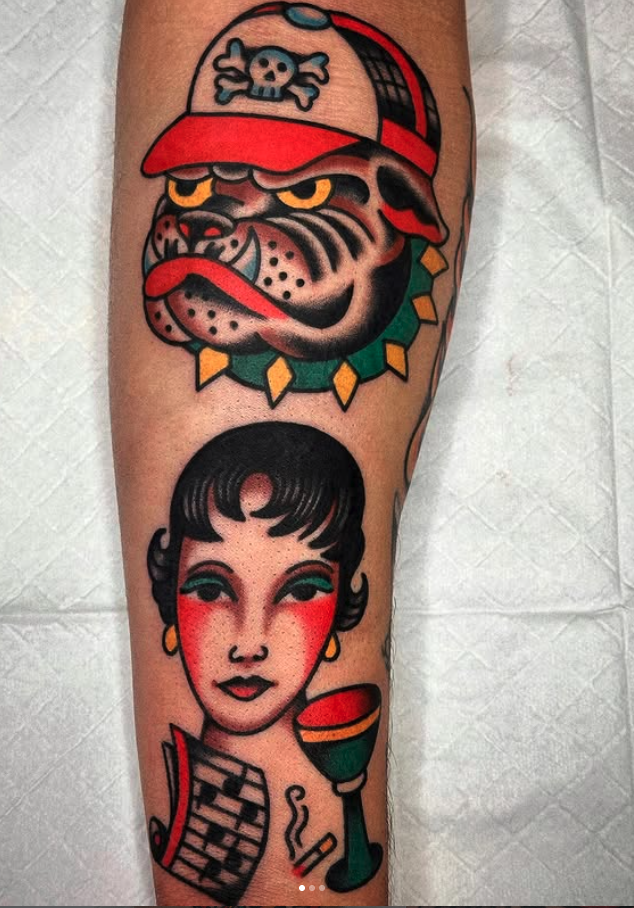 Tattoo of a woman with short black hair, green eyeshadow, and red cheeks, holding a wine glass. Above, a tiger wearing a red cap with a skull and crossbones symbol, with a yellow, green, and black collar around its neck.