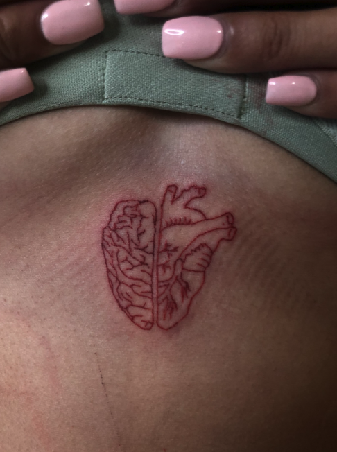 A tattoo of a human heart, with one side depicted as an anatomical heart and the other side as a brain, on a person's skin near the collarbone.