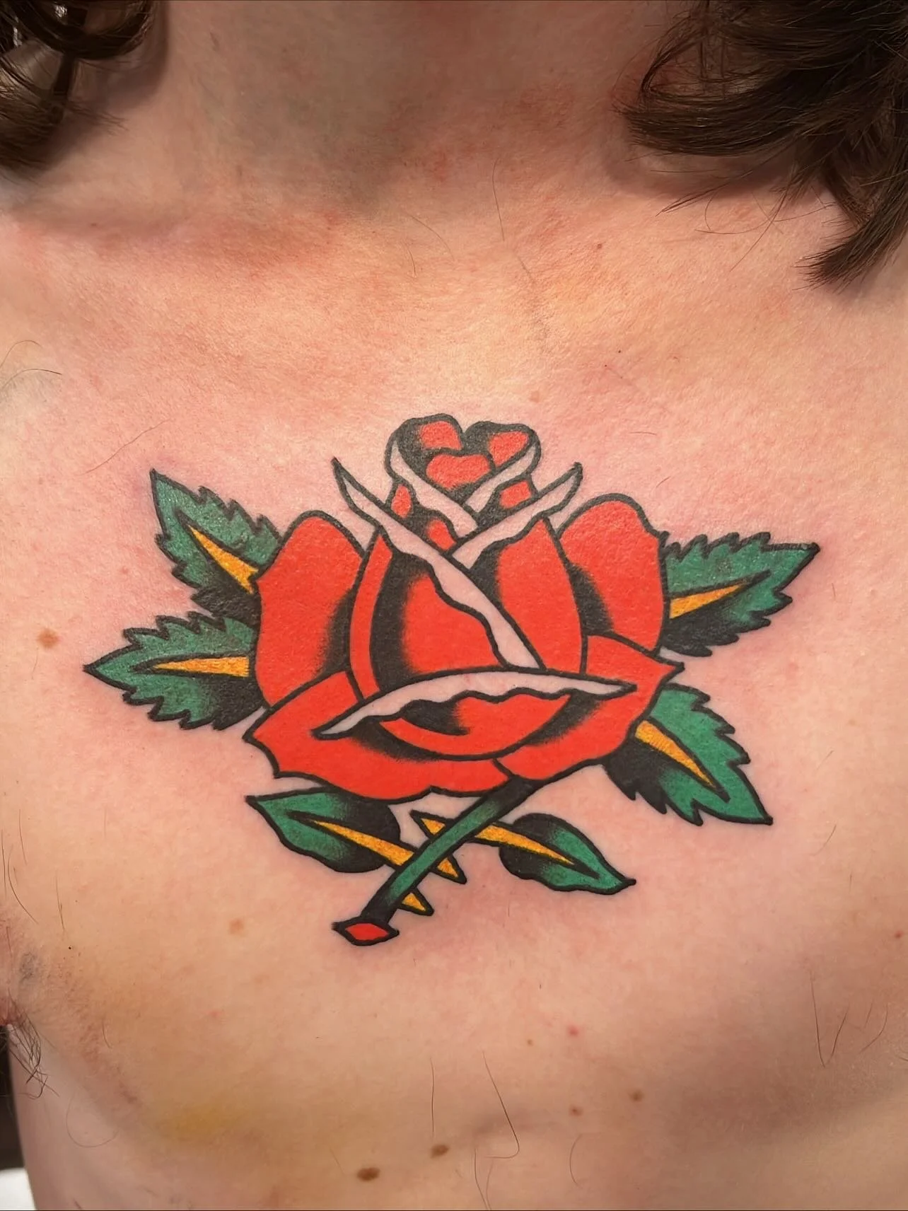 Tattoo of a red rose with a dagger through it on a person's chest.