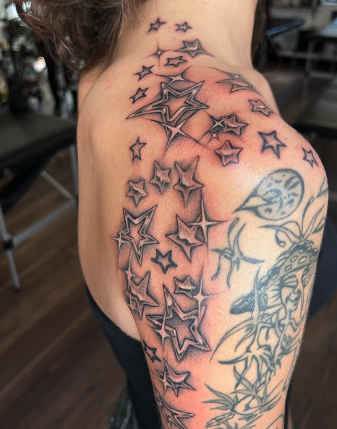 Tattoo of stars on a person's shoulder and upper arm with a moon and plant design.