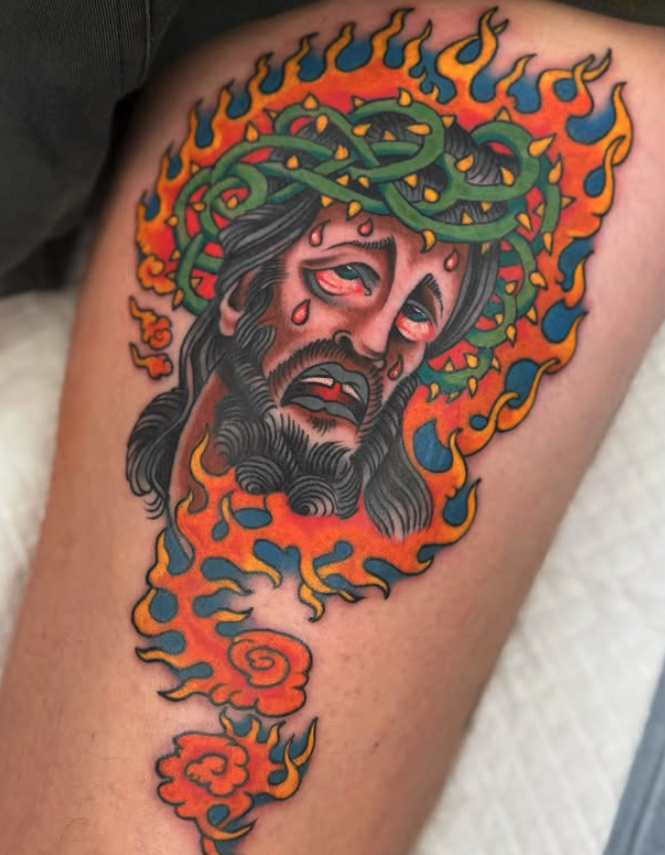 Tattoo of Jesus Christ's face with a crown of thorns, tears, and a crown of thorns on his head, surrounded by flames and smoke in vibrant colors.