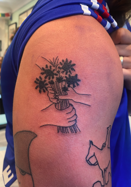 Tattoo of a hand holding a jar of flowers on a person's upper arm.