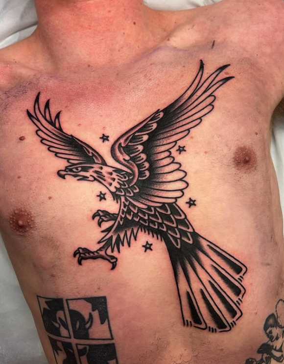 Tattoo of an eagle in flight with stars around it on a person's chest.