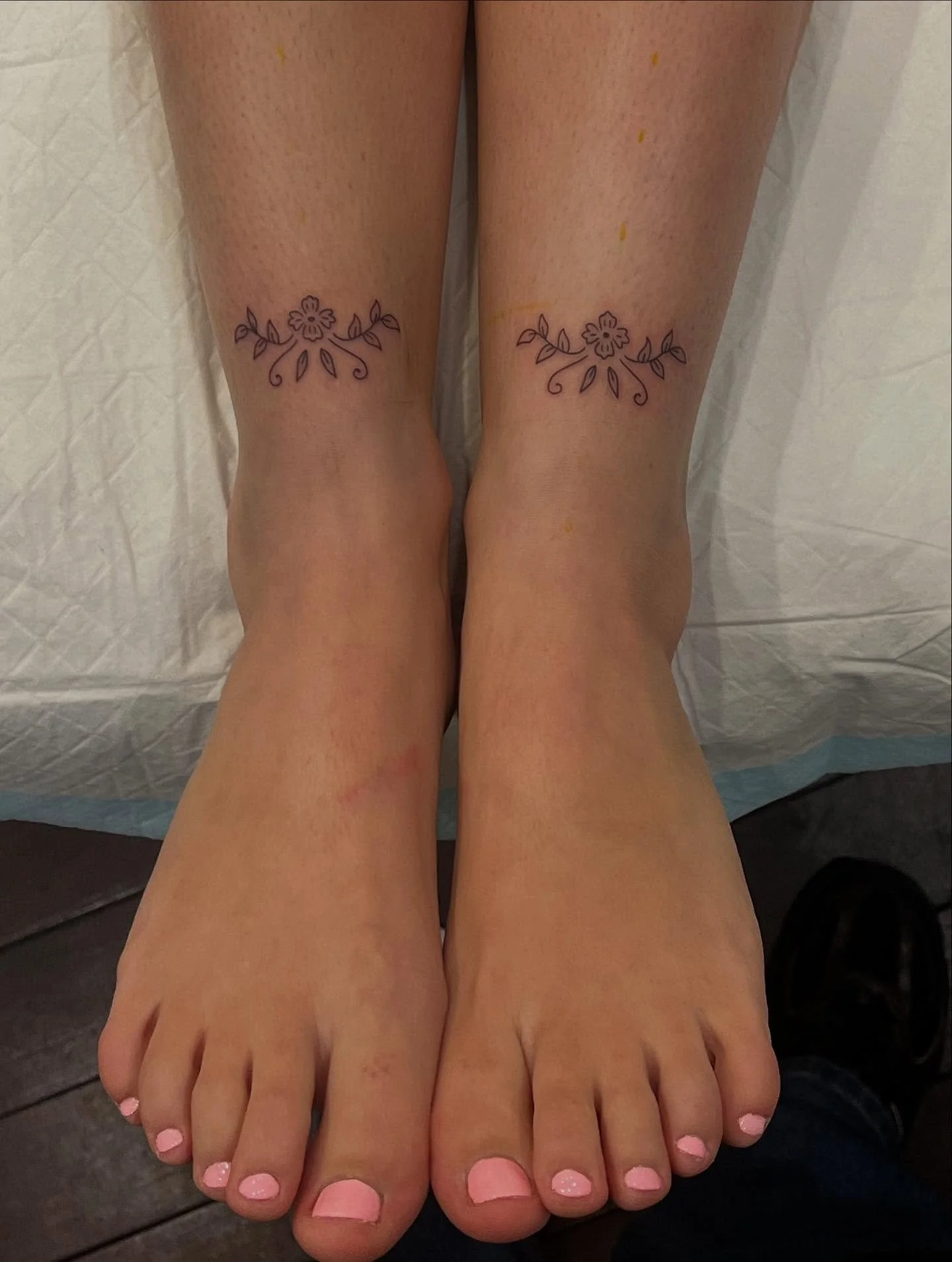 A pair of feet with pink painted toenails and matching floral tattoos just above the ankles.