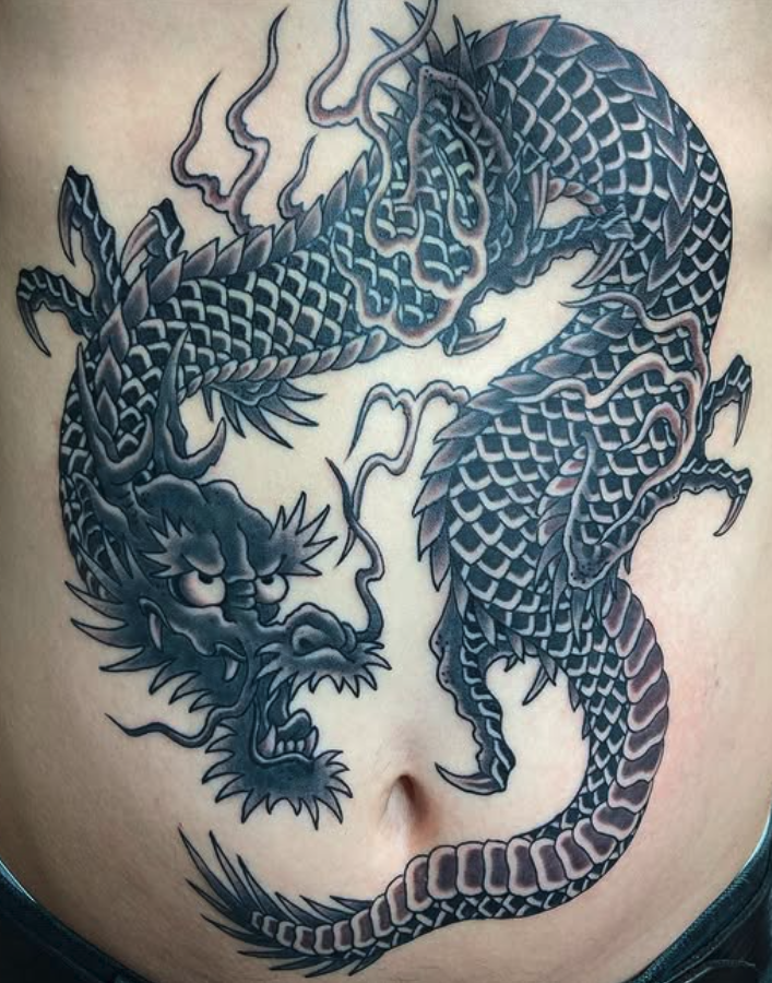 Tattoo of a fierce dragon with scales, horns, and claws, depicted in black and gray ink, wrapping around the person's abdomen.