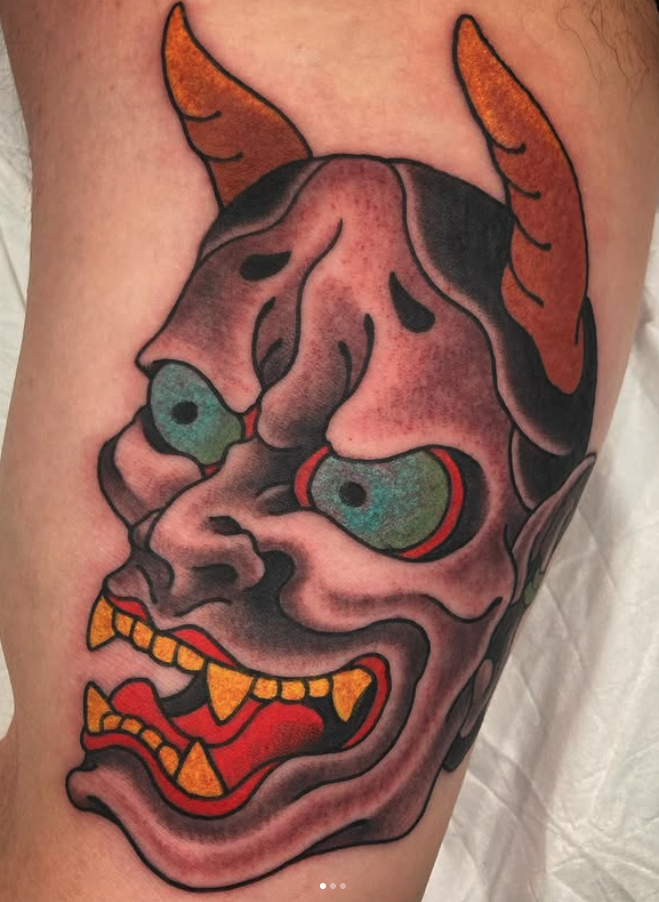 Tattoo of a demonic clown face with horns, exaggerated facial features, and sharp teeth.