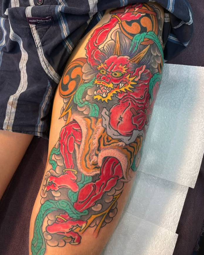 Colorful Japanese-style dragon tattoo on a person's leg with red, orange, green, and yellow hues.
