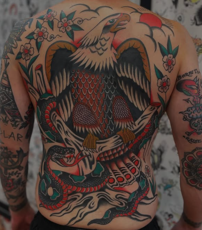 Traditional-style tattoo of an eagle with outspread wings, perched on a branch, with a snake coiled below it on the person's chest.