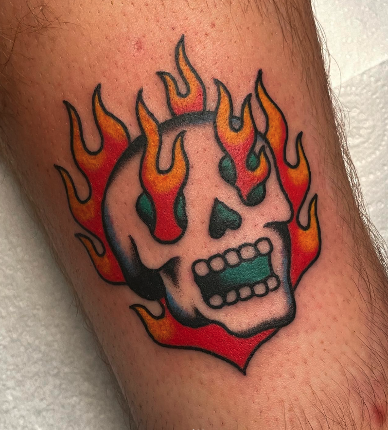 Tattoo of a skull with flames around it, in traditional tattoo style.