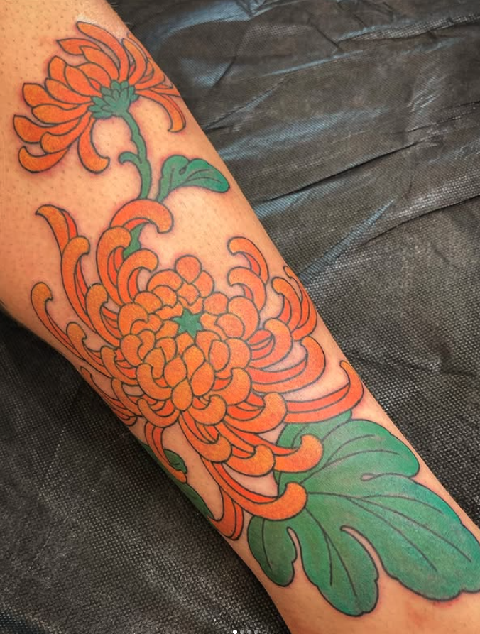 Tattoo of orange chrysanthemums with green leaves on a person's arm.