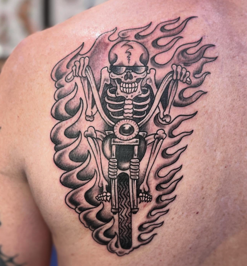 Tattoo of a skeleton riding a motorcycle with flames in the background.