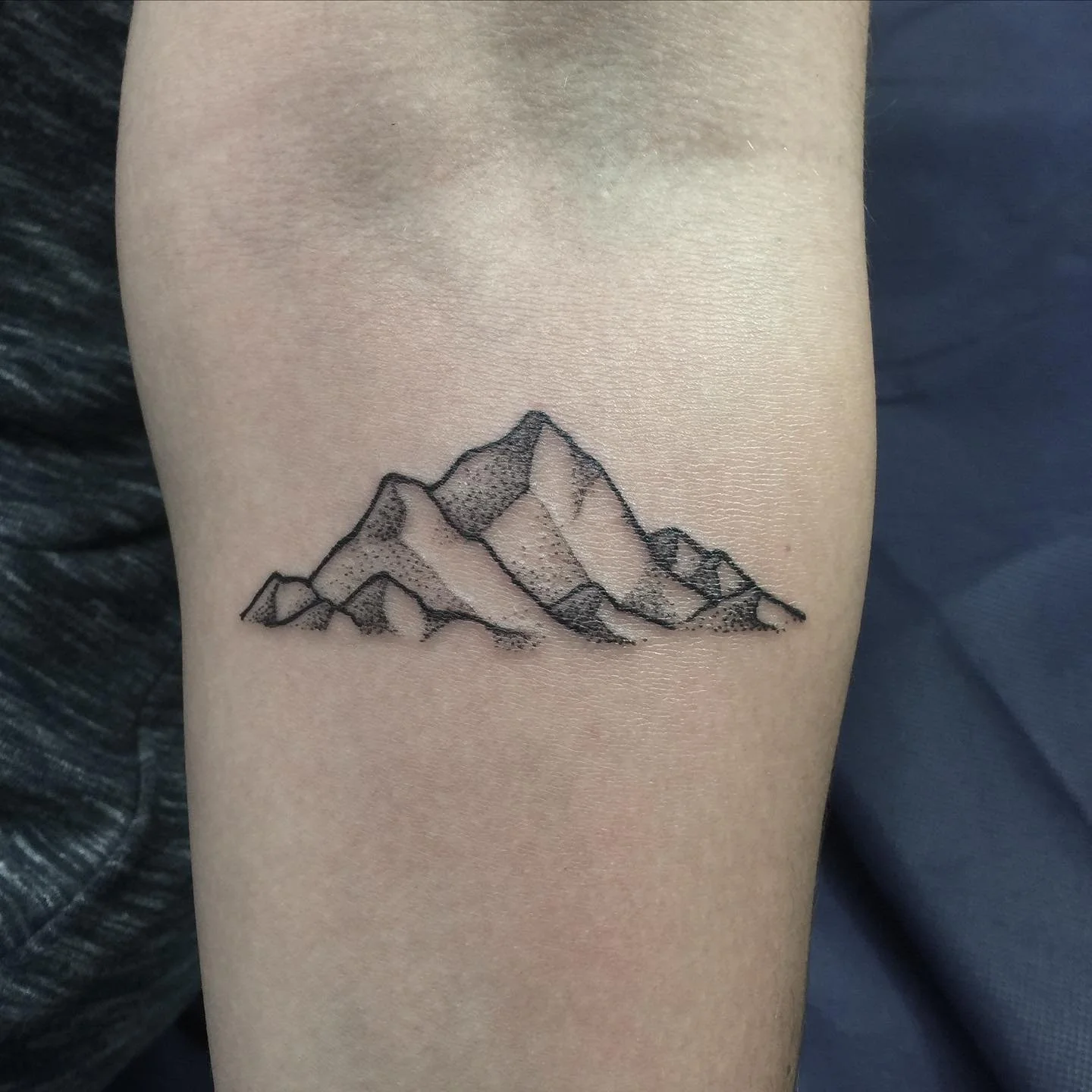 Black outline tattoo of mountain range on skin.