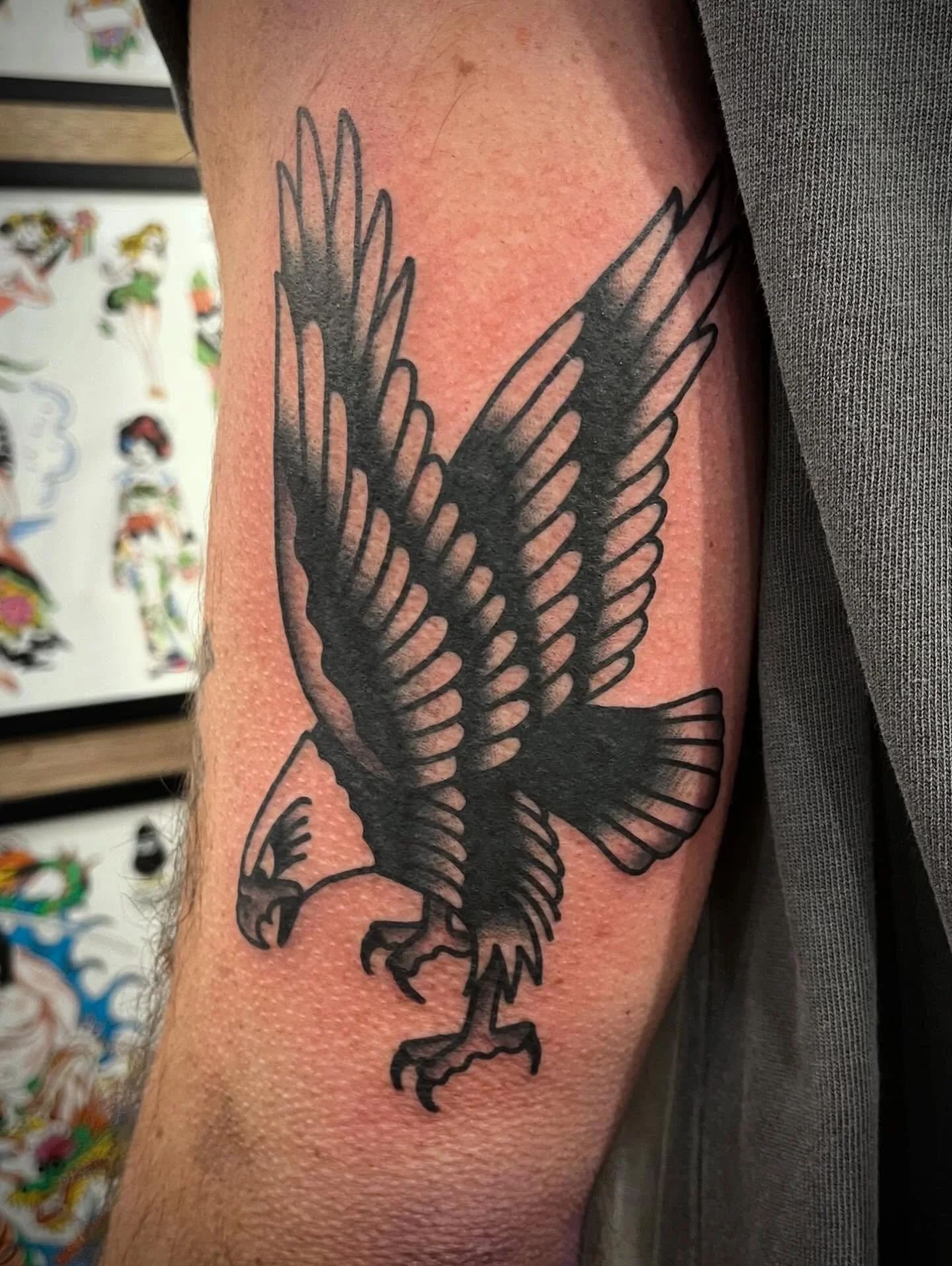 Black outline tattoo of an eagle with wings spread, positioned on the upper arm.