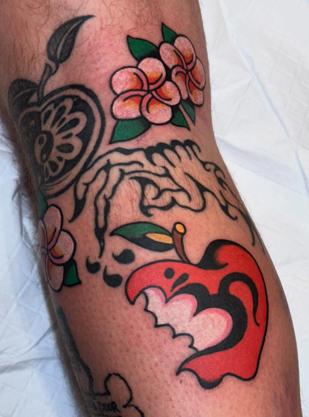 Tattoo of pink flowers, green leaves, and a red stylized devil's face on a person's arm.