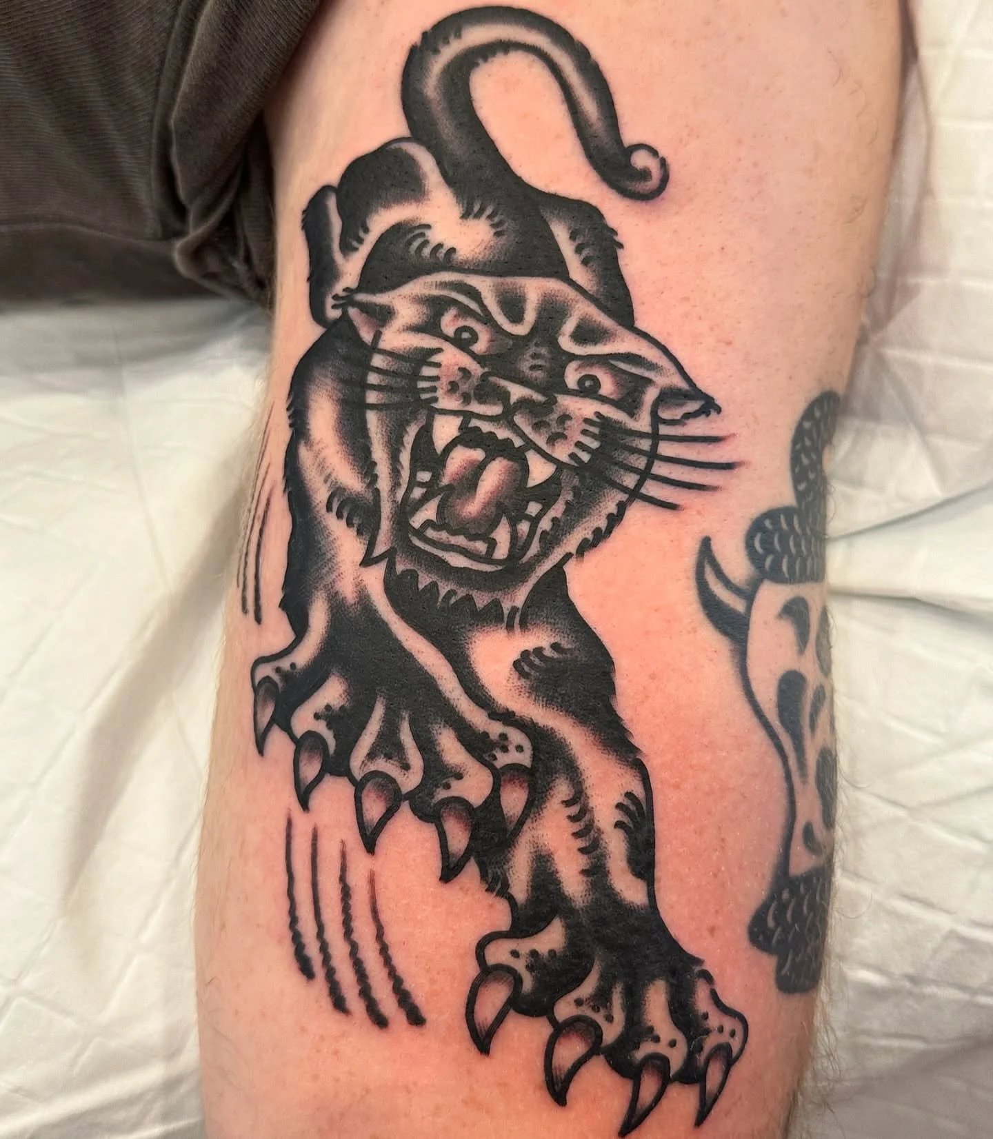 Tattoo of a cartoonish panther with an open mouth showing sharp teeth, standing with claws extended.