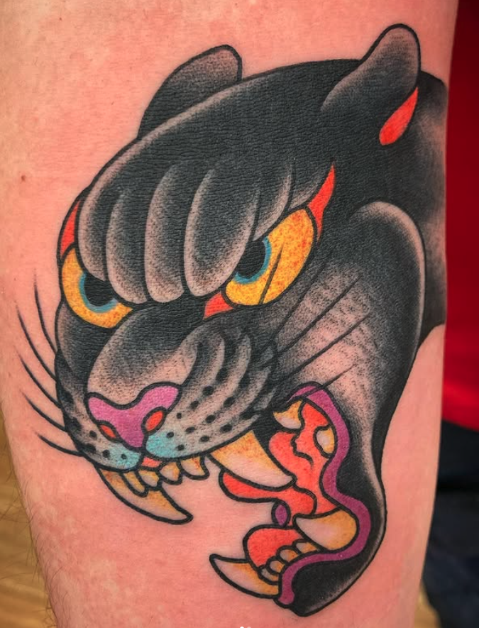 Close-up of a colorful tattoo of a panther's face and paw, with prominent yellow eyes and open mouth showing teeth, on skin.