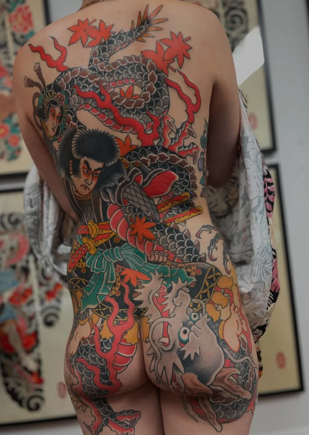 A person with an elaborate traditional Japanese-style tattoo covering their back and buttocks, featuring a dragon, a warrior, and various decorative elements.
