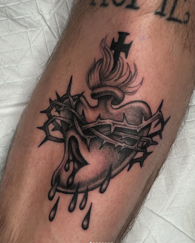 Tattoo of a broken heart with barbed wire wrapped around it, drops of blood, and a small flame with a cross on top.