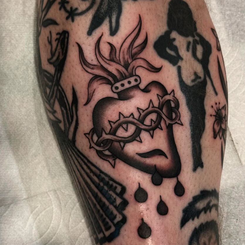 Tattoo of a stylized heart with a chain and a crown of thorns around it, teardrops falling from the lips, and flames emerging from the top.