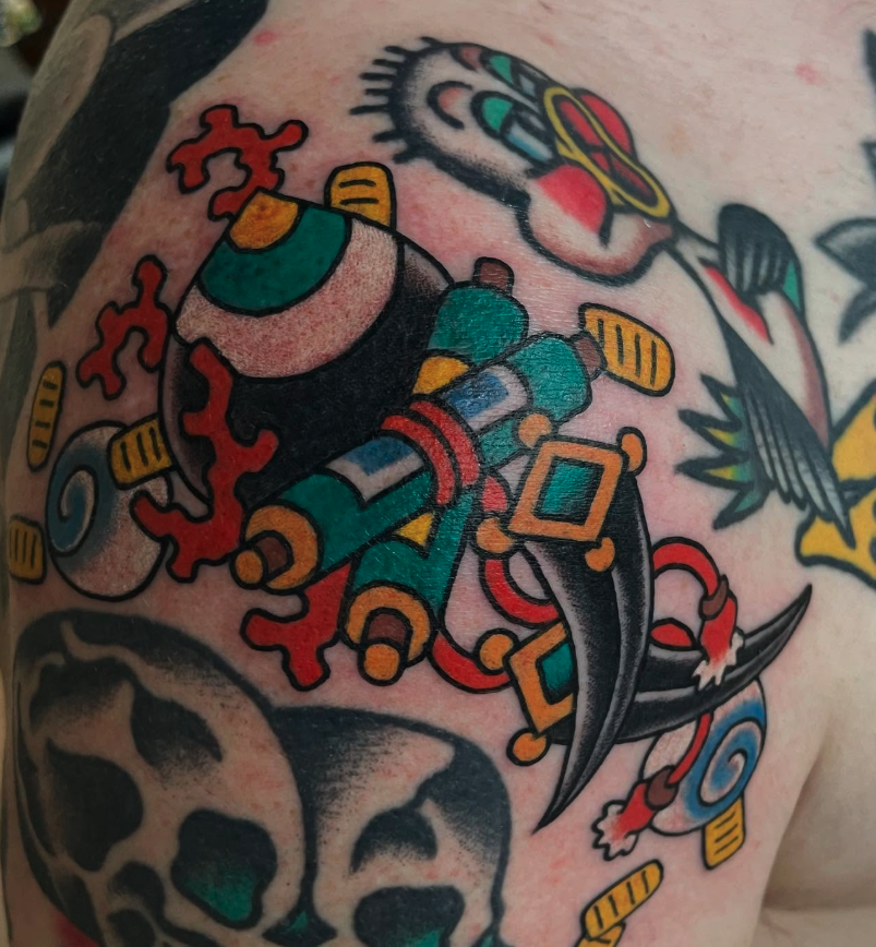 Colorful tattoo featuring a detailed tattoo gun with vibrant colors, skulls, and various decorative elements.