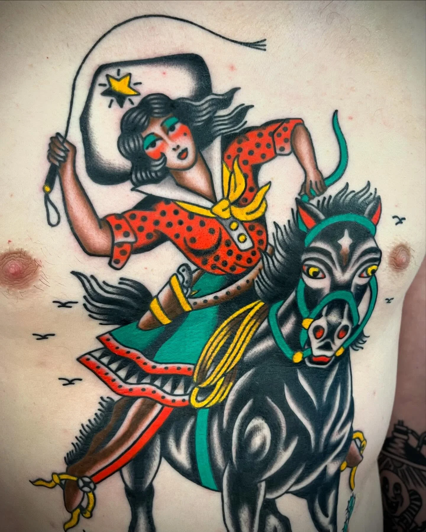 A colorful tattoo of a woman riding a black horse, holding a whip, with vibrant clothing and detailed features.